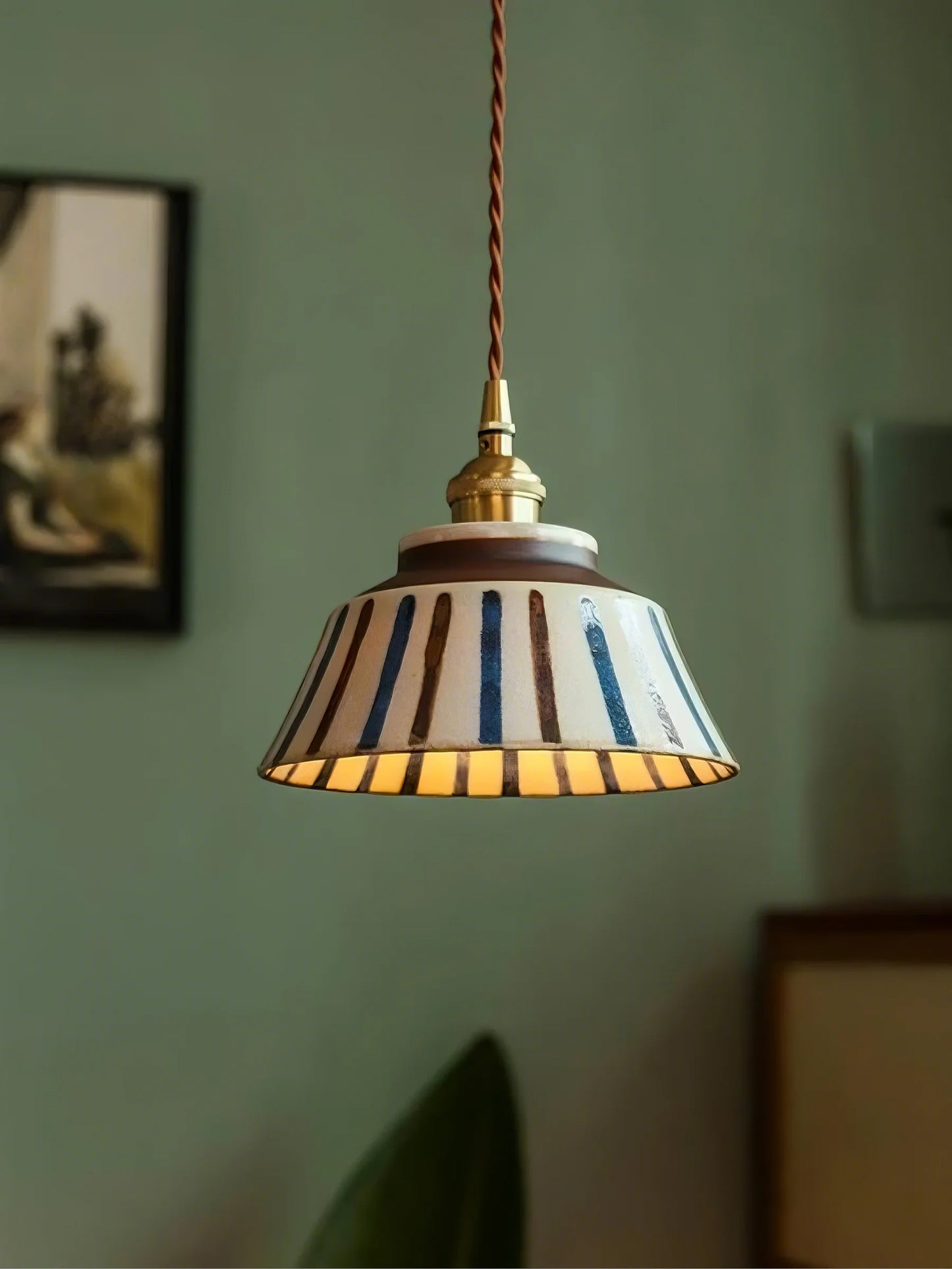 Pendant light with striped shade hanging against a green wall.