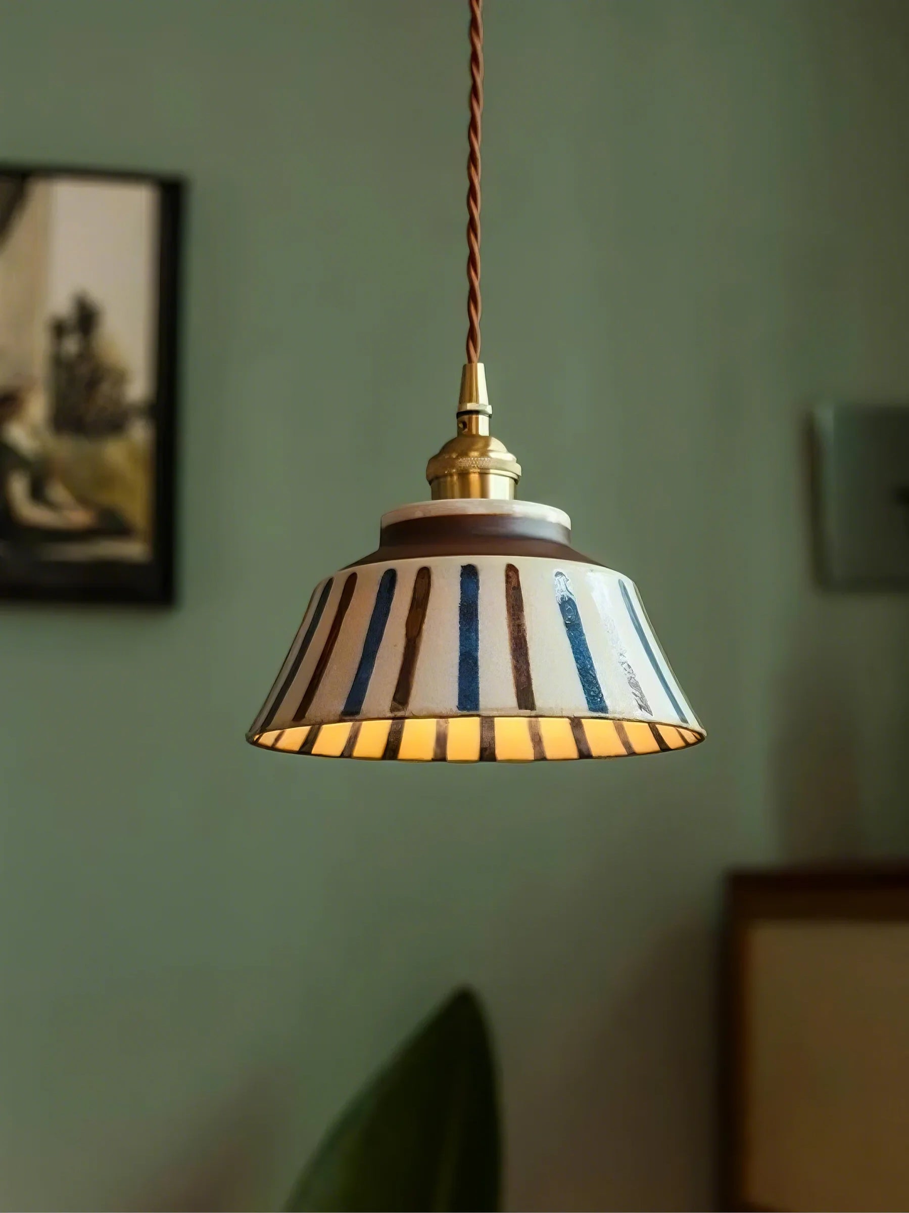 Pendant light with striped shade hanging against a green wall.