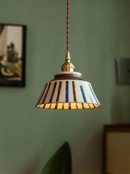 Pendant light with striped shade hanging against a green wall.