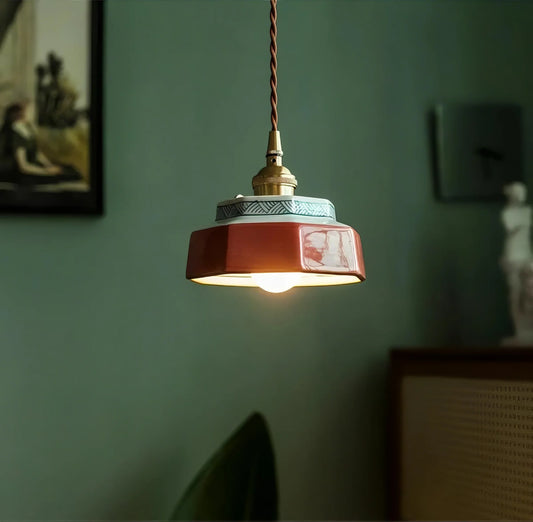 Red pendant light with a gold bulb holder against a green wall.