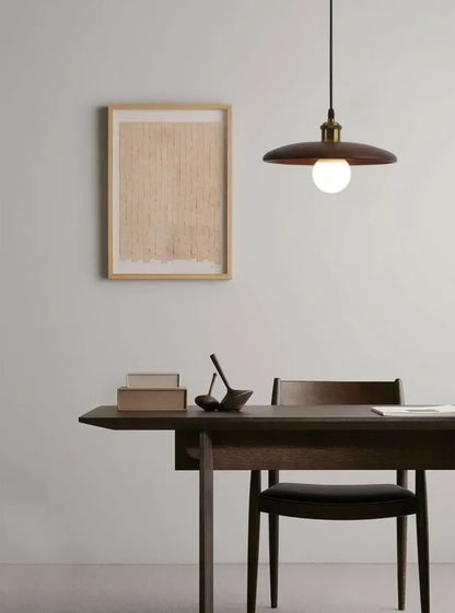 Modern dining room with wooden table, chairs, and pendant light against a plain wall.