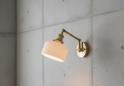 Wall-mounted lamp with a beige shade and gold arm on a concrete wall.