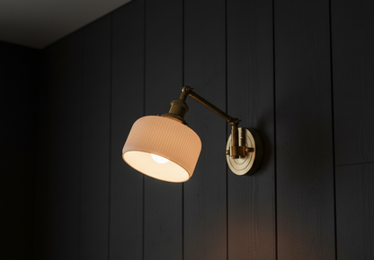 Wall-mounted lamp with a beige shade and gold fixture on a dark wooden panel wall.