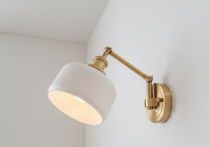 Wall-mounted lamp with white shade and gold arm on a light gray wall.