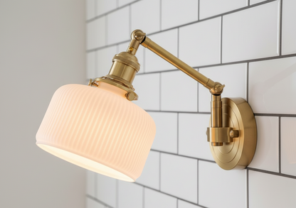 Wall-mounted lamp with a brass arm and white shade against a tiled wall.