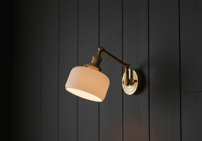 Wall-mounted lamp with a beige shade and gold arm against a dark wooden panel background