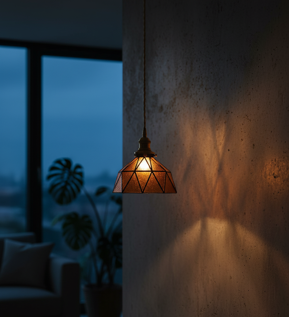 Geometric pendant light casting a warm glow against a dark wall with a blurred indoor background