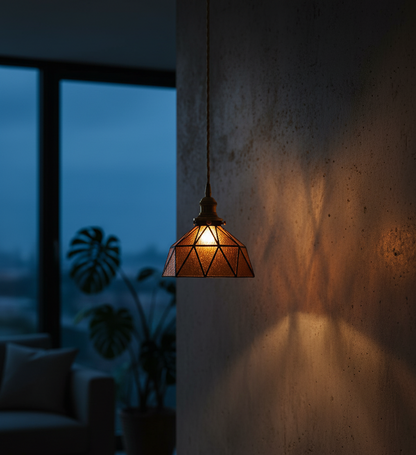 Geometric pendant light casting a warm glow against a dark wall with a blurred indoor background